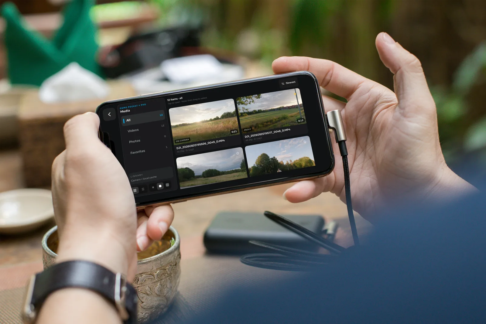 OpenPocketCine media library on iPhone: all clips, videos, photos, and favorites over a cafe table